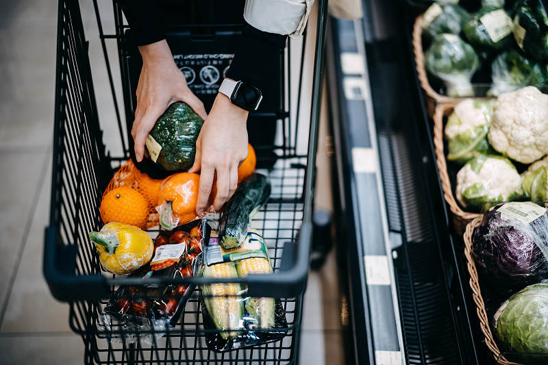 近距离的女人的手在超市购买新鲜的食品杂货，并把各种有机蔬菜在购物车图片素材