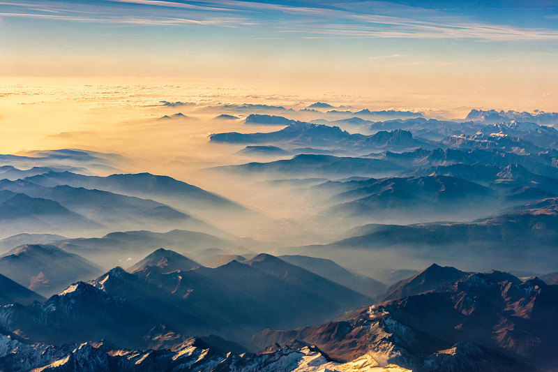 从飞机上俯瞰，透过云层从山顶俯瞰美丽的山景。图片素材