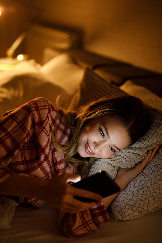 年轻漂亮的女人晚上在床上玩手机图片下载