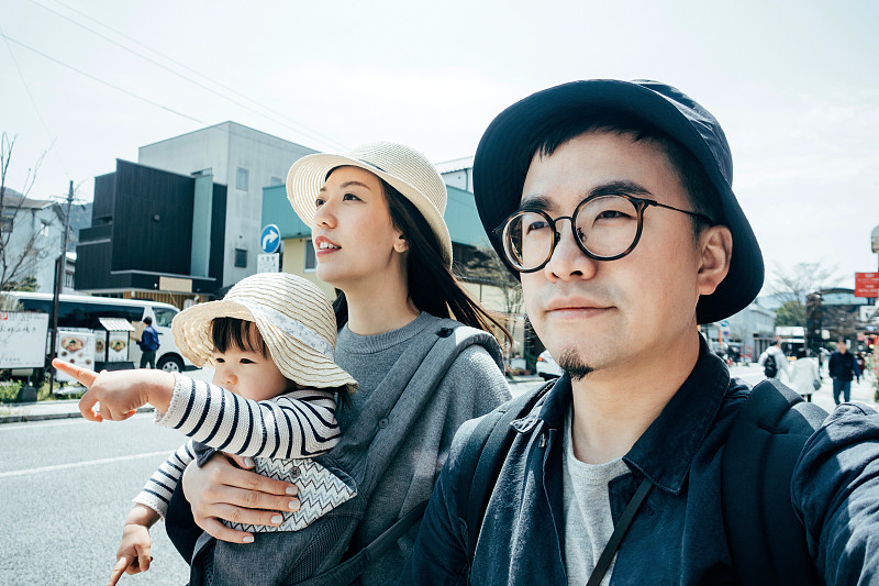 在一个阳光明媚的日子里，快乐的年轻亚洲三口之家正在日本福冈的一个当地小镇游玩和探索图片下载