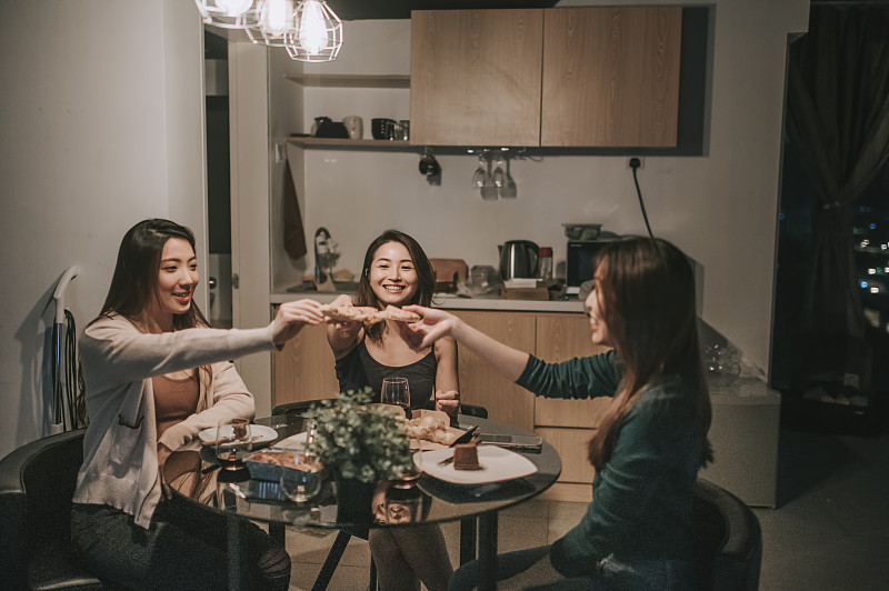 一群亚裔中国女性朋友在公寓里社交聚会，晚上在餐厅吃披萨图片素材