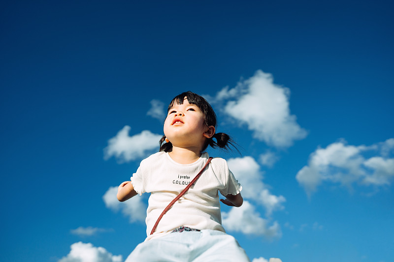 快乐的亚洲小女孩开心地微笑着举起她的双手，想象在一个可爱的阳光明媚的日子里在美丽的蓝天飞翔图片素材