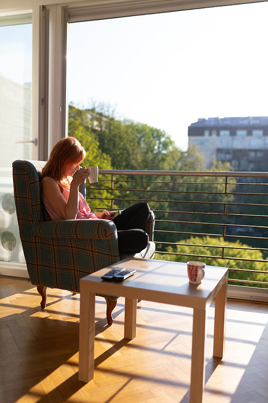 坐在露天阳台扶手椅上的女人一边喝着咖啡，一边望着外面图片下载