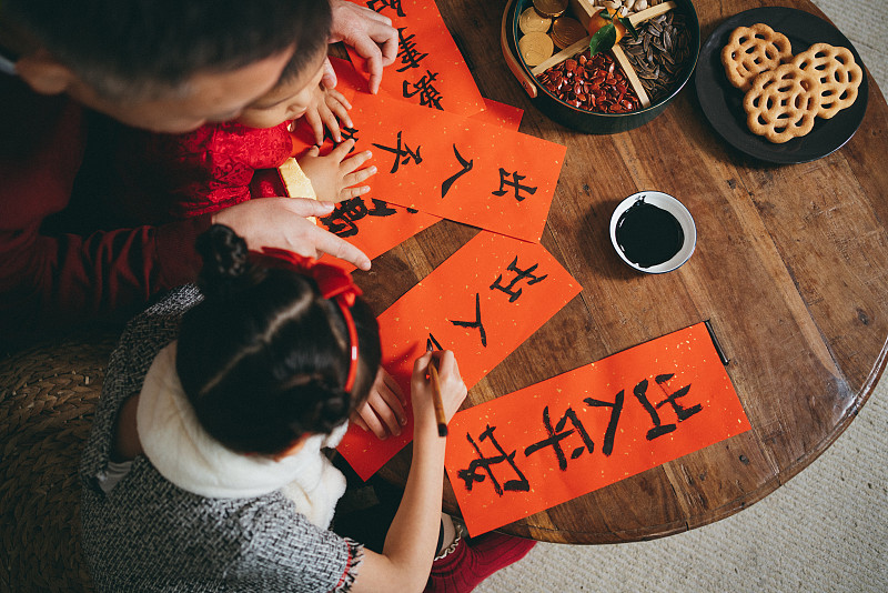 Overhead view of joyful little granddaughter and grandson practising Chinese calligraphy for Chinese New Year on couplets with their grandfather图片素材