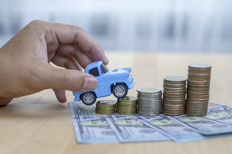 近手握模型的玩具汽车上叠硬币-保险，贷款和购买汽车金融的概念。图片素材