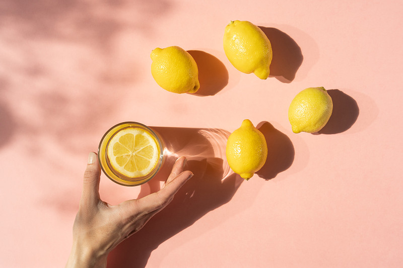 特写手与喝的杯子和柠檬在粉红色的背景图片素材