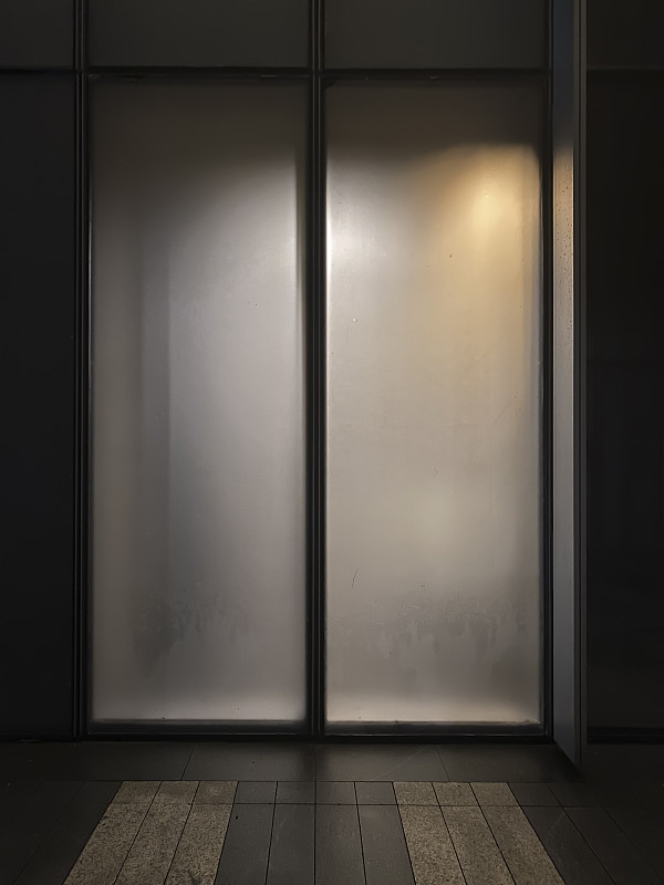晚上，室内灯光透过办公大楼的玻璃门照射进来图片素材