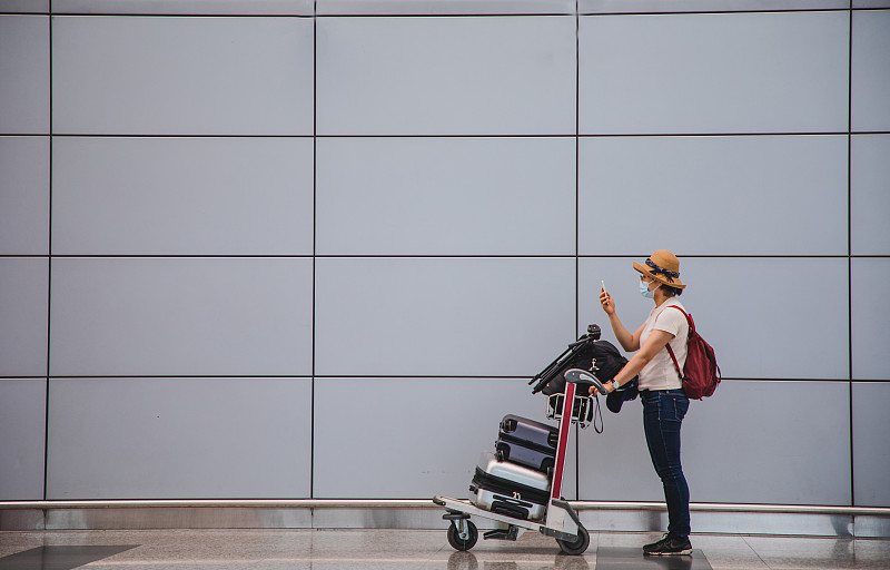 一名亚洲妇女推着行李车在机场候机厅打电话图片素材