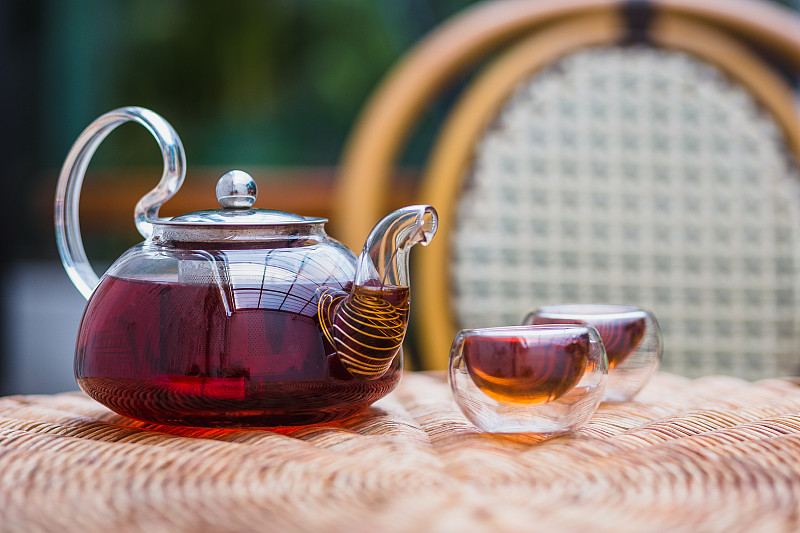 一个玻璃茶壶和茶杯放在家里的藤桌上，茶道概念图片下载