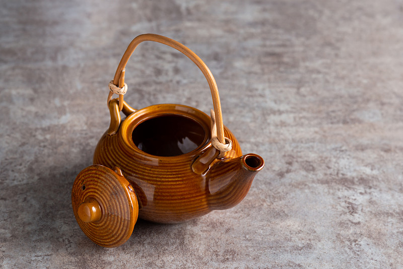 一个棕色的茶壶，竹柄和一个打开的盖子在一个石头台面上。copyspice图片下载