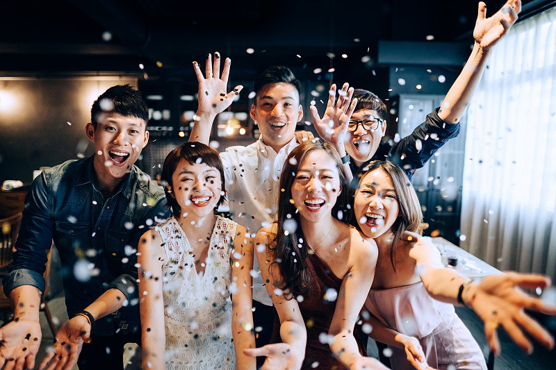 一群年轻的亚洲男人和女人在派对上玩得很开心，吹着闪闪发光的纸屑图片下载