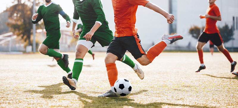 成人足球运动员跑后球和踢联赛。决斗中的一组球员。穿着橙色和绿色运动衫的足球运动员图片下载