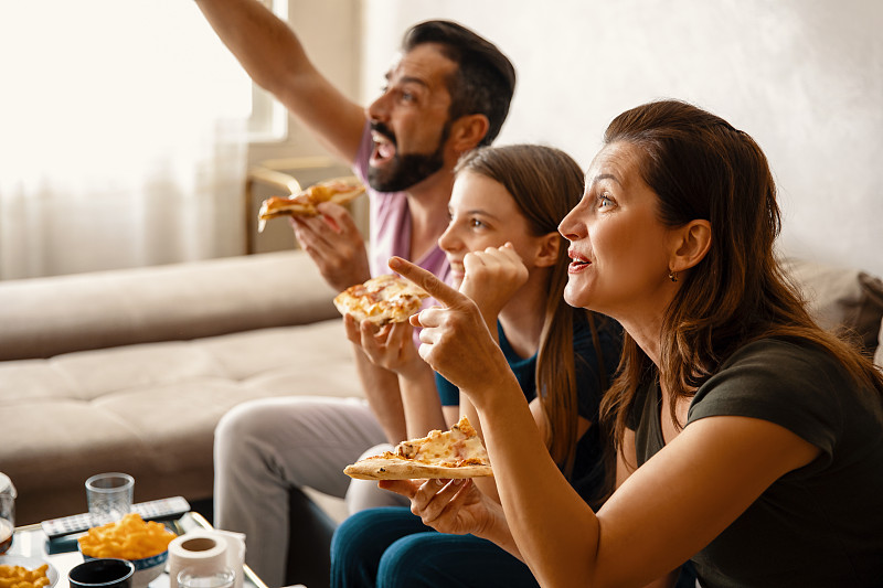 一家人吃着披萨，在电视上看最喜欢的体育节目图片下载