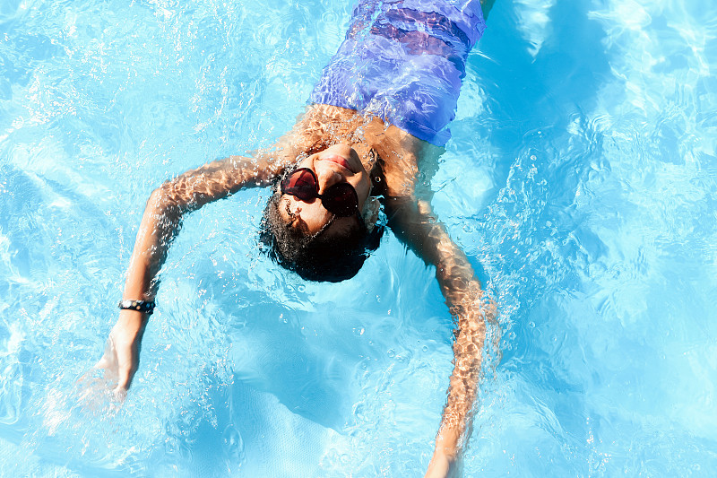 一个皮肤黝黑的少女在游泳池里游泳。活泼有趣的消遣为孩子。夏天。暑假。假期。图片下载