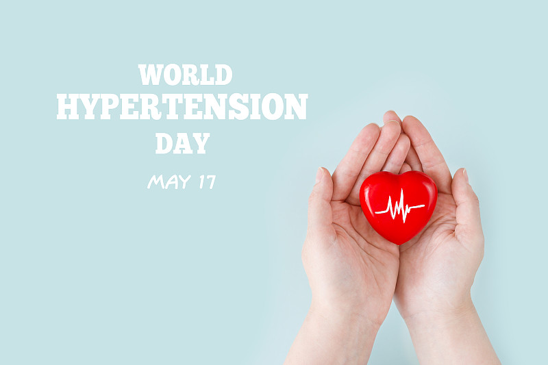 世界高血压日。女人的手握着一颗红色的心，用手握着心跳图——高血压的象征。5月17日高血压日。世界心脏日，世界卫生日。图片下载