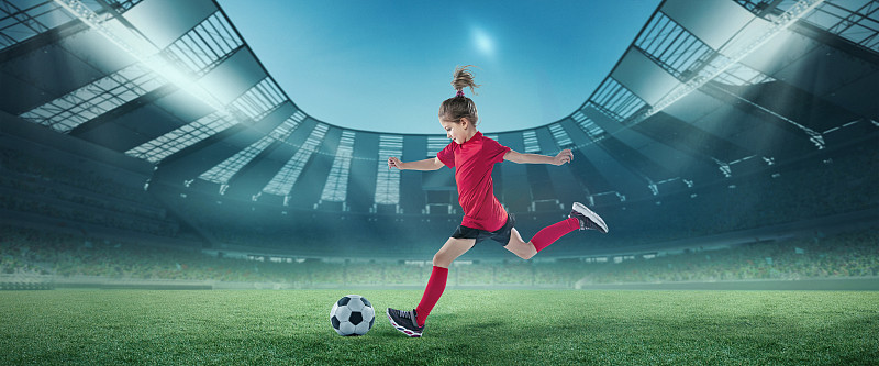 活泼的女孩，在运动中穿着红色制服的足球运动员，在露天体育场击球。冠军图片下载