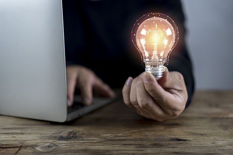 商人拿着发光的灯泡放在木桌上，手提电脑作为商业解决方案图片下载
