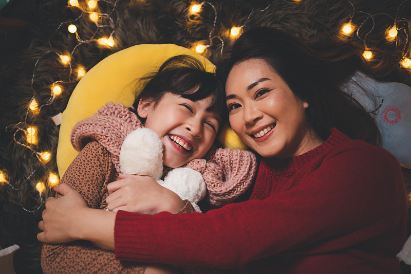在神奇的夜晚，快乐的亚洲母亲给女儿们讲故事。阖家欢乐的圣诞和新年假期概念。图片下载