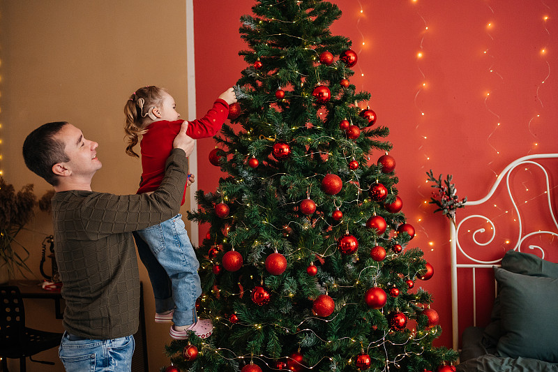 爸爸用人工耳蜗把女儿高高举起，用玩具装饰圣诞树图片下载