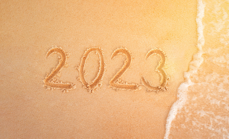 2023年沙滩上的人物背景是除夕夜。海浪冲走了黄沙上的铭文2023。新年假期在海滩上。图片下载