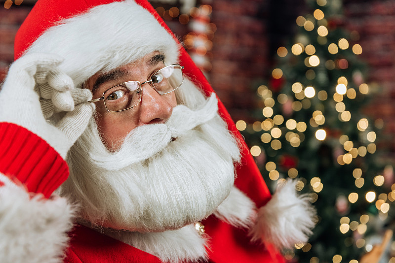 圣诞老人戴着眼镜的特写肖像，在一棵圣诞树的背景下看着相机图片下载