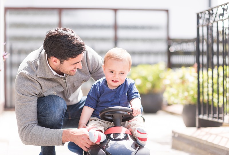 爸爸和小儿子在一起玩，儿子骑着玩具车图片下载