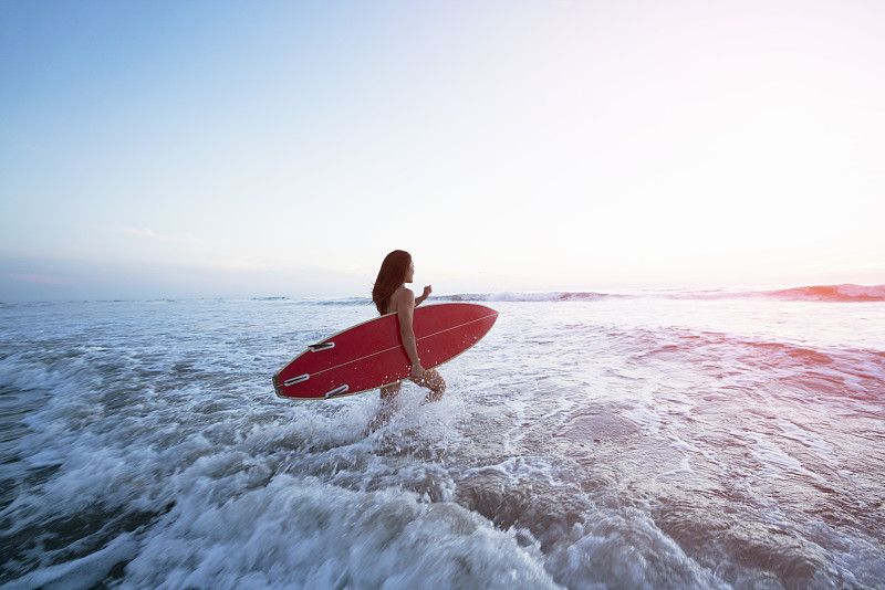 一个年轻女人拿着冲浪板走进了海浪图片素材