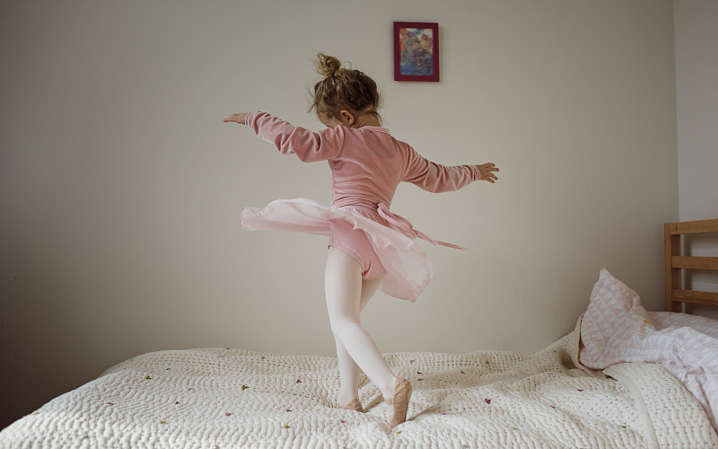 穿着芭蕾服装的女孩在家里的床上跳舞图片下载