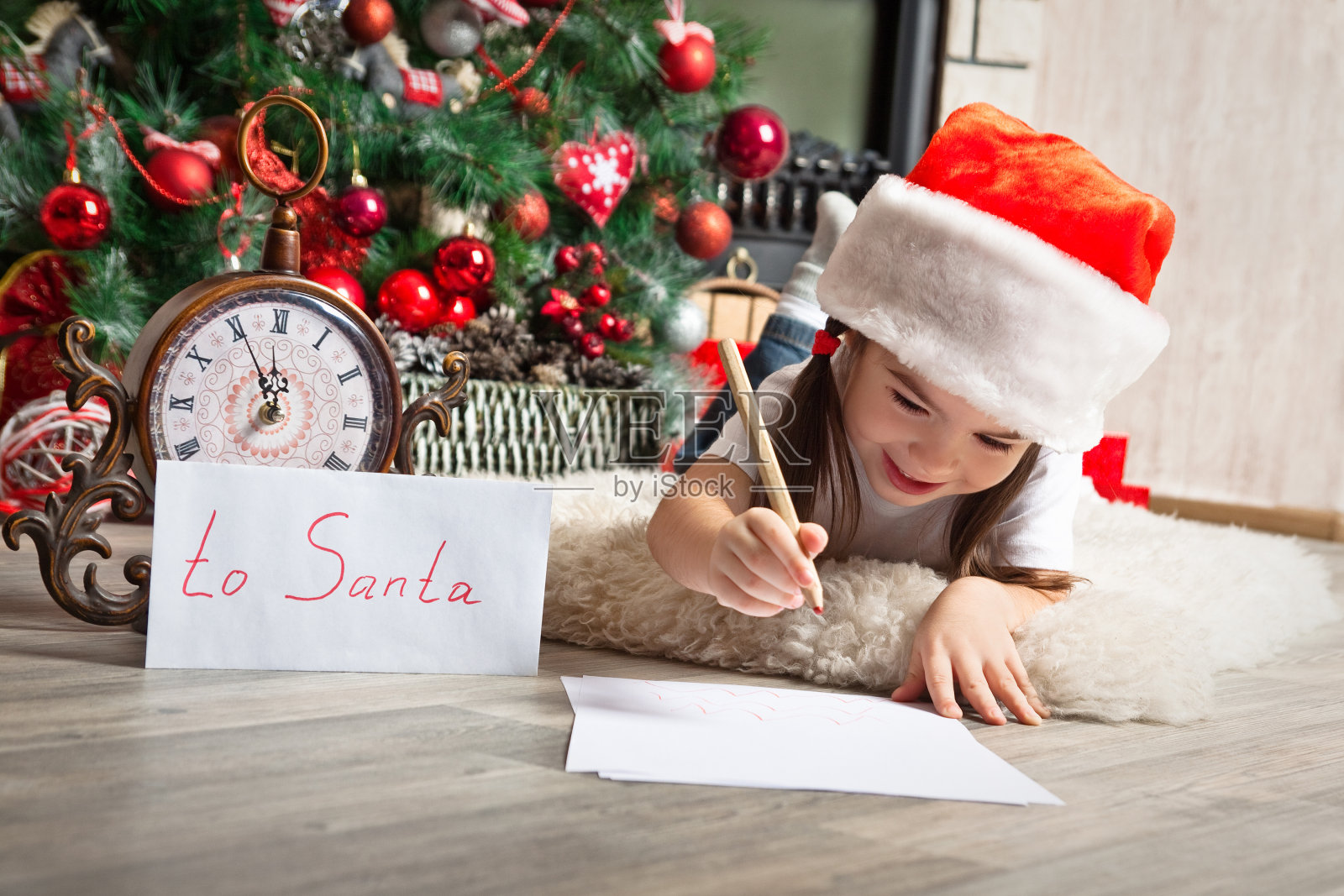 漂亮的小女孩戴着圣诞帽给圣诞老人写信照片摄影图片