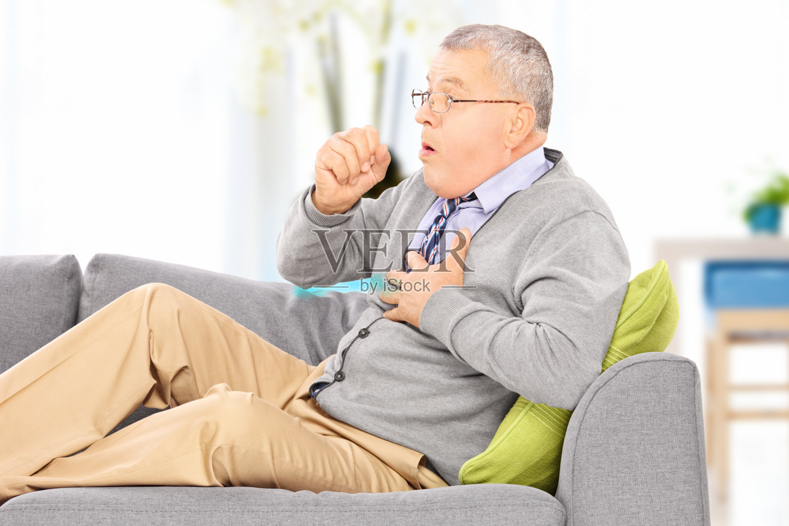 一个成熟的病人坐在灰色的沙发上咳嗽照片摄影图片