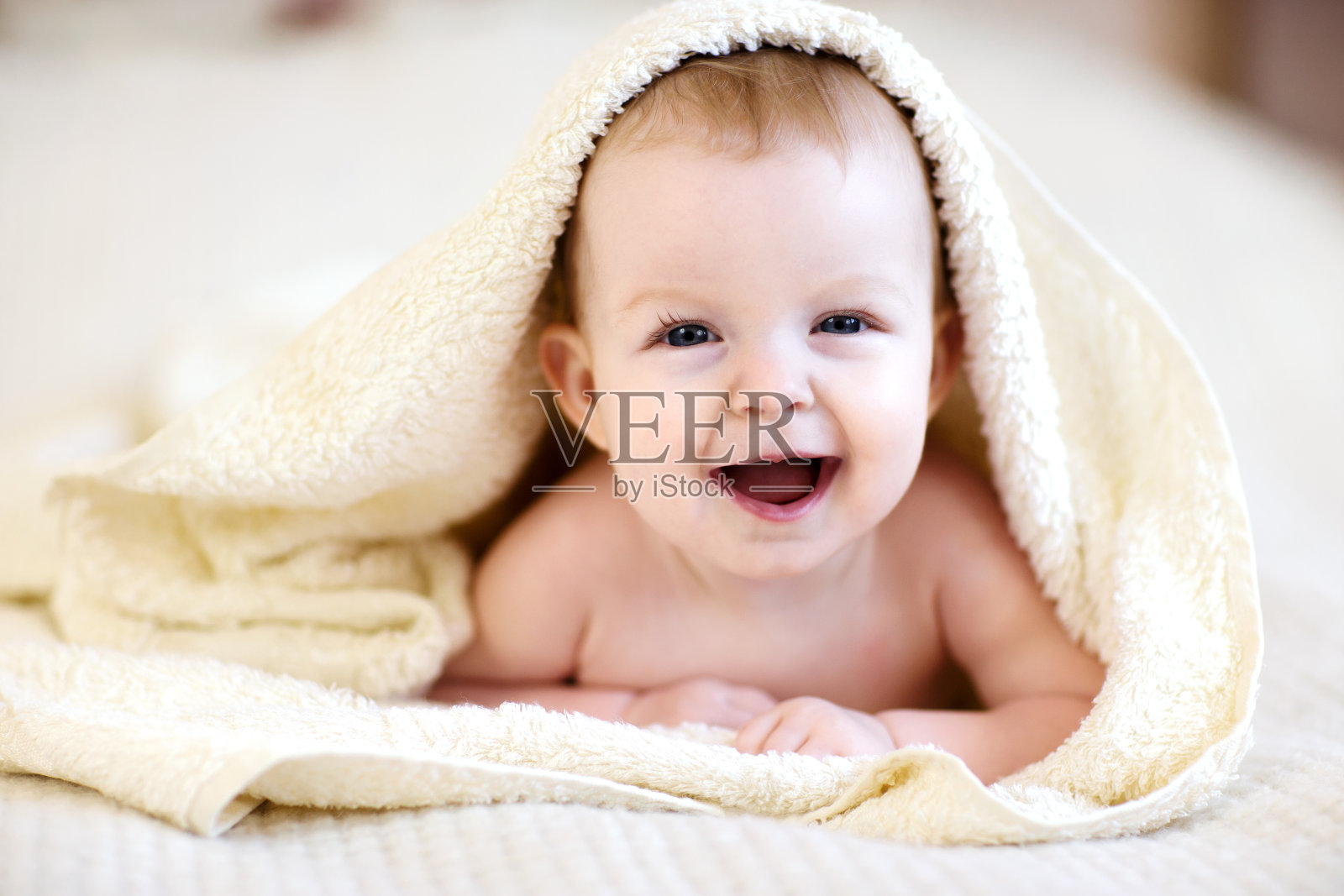 笑着的宝宝裹着毛巾躺在床上照片摄影图片