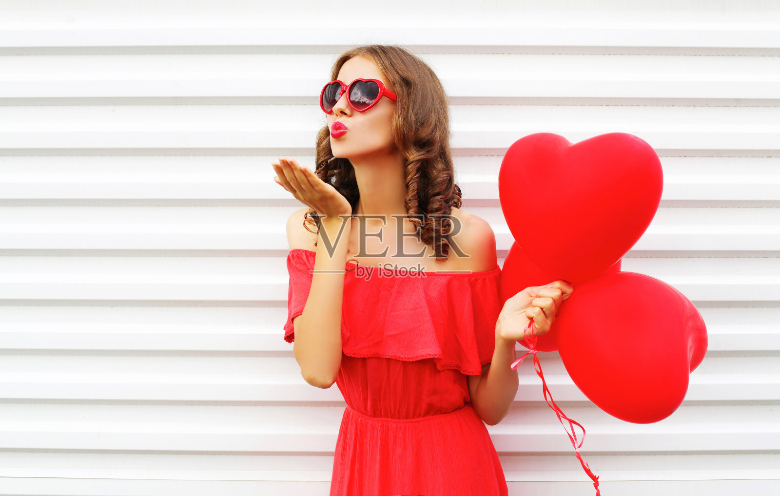 肖像女人在红色的裙子送气球心形的空中吻白色的背景照片摄影图片