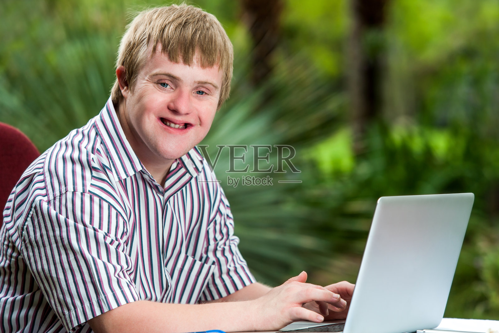 一个在花园里用笔记本电脑打字的残疾年轻人。照片摄影图片