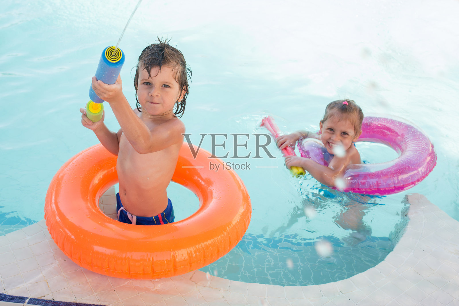 两个孩子在游泳池里玩塑料玩具枪。照片摄影图片