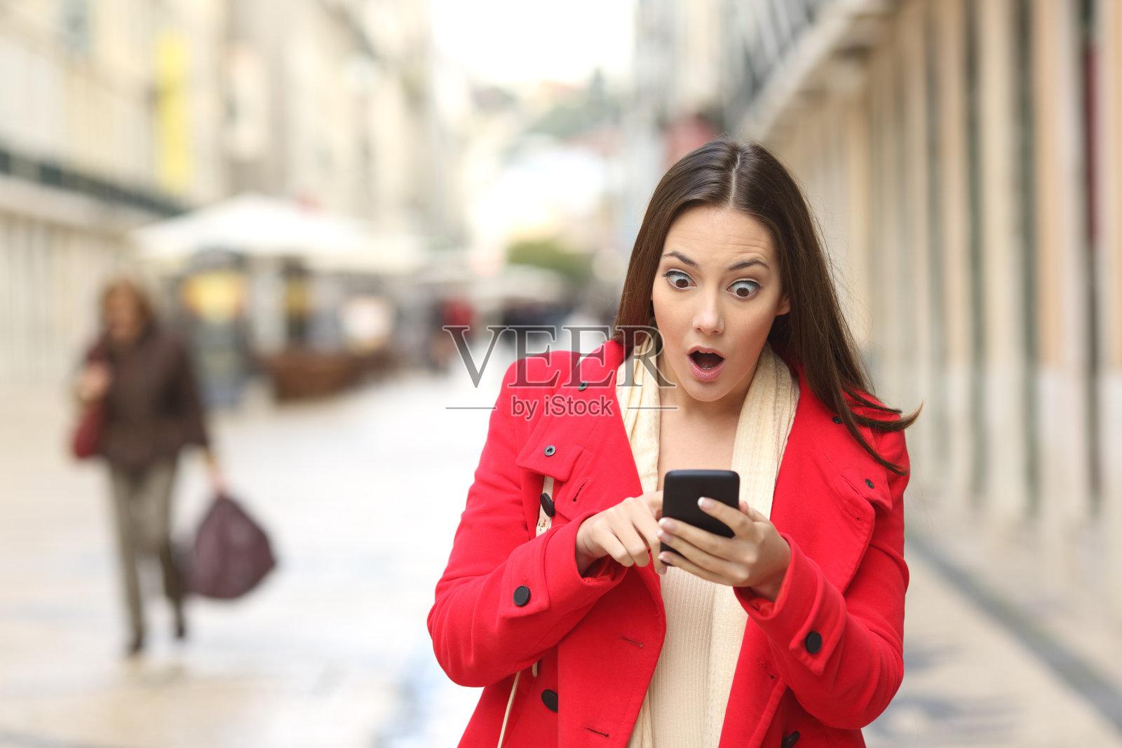 惊讶的女人在街上查看智能手机照片摄影图片