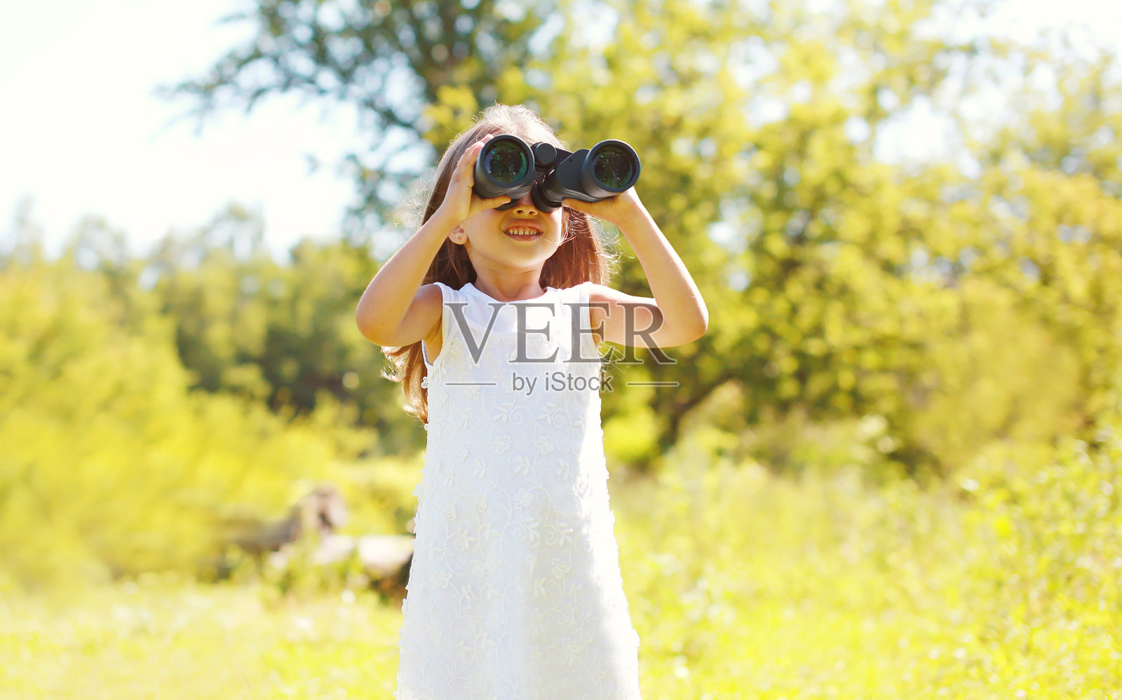 小女孩在夏天用双筒望远镜看照片摄影图片