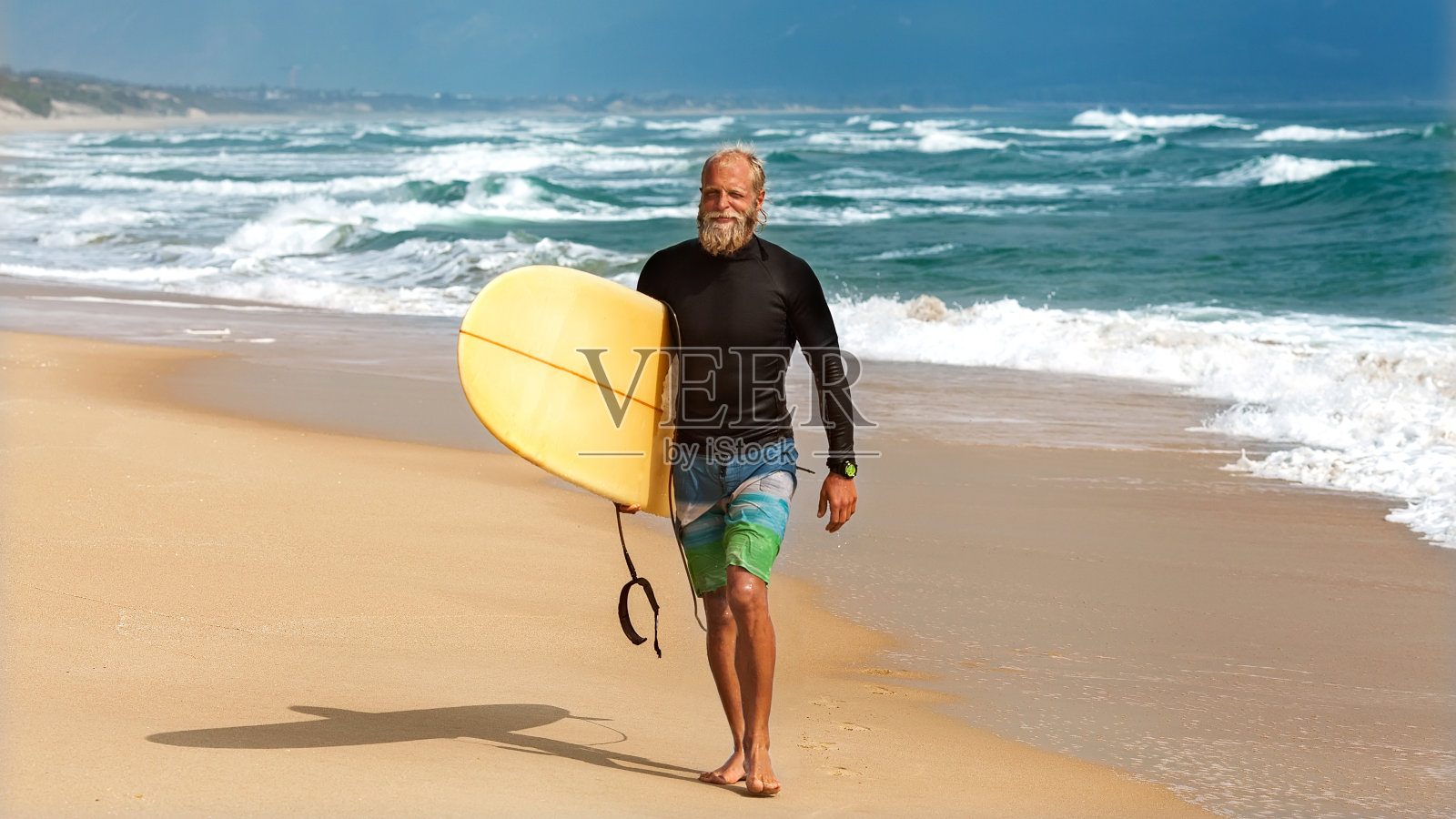 一个冲浪者站在海边，手里拿着冲浪板照片摄影图片
