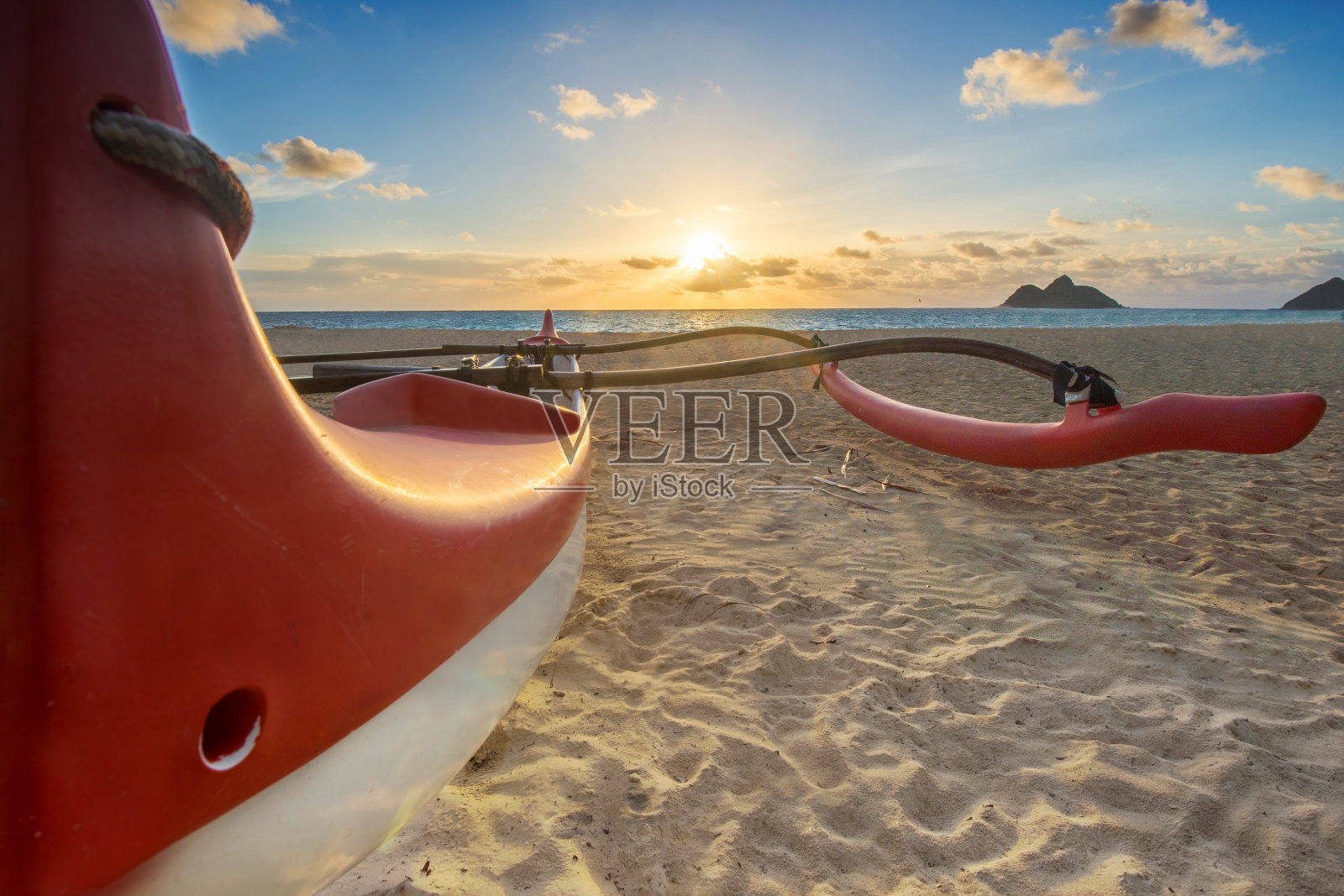 日出时海滩上的红色和白色的支腿独木舟照片摄影图片