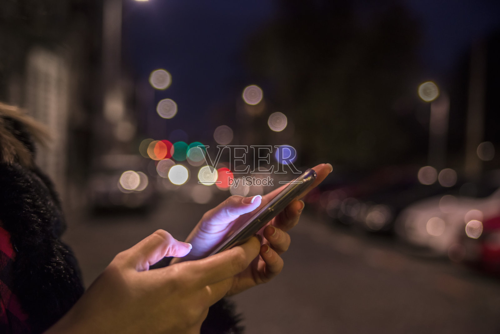 女性手握手机触摸屏上模糊不清的夜灯照片摄影图片