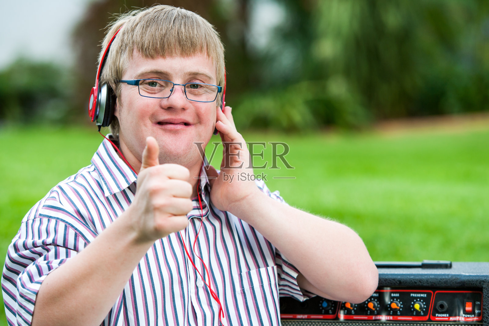 戴着耳机的唐氏综合症男孩竖起大拇指。照片摄影图片