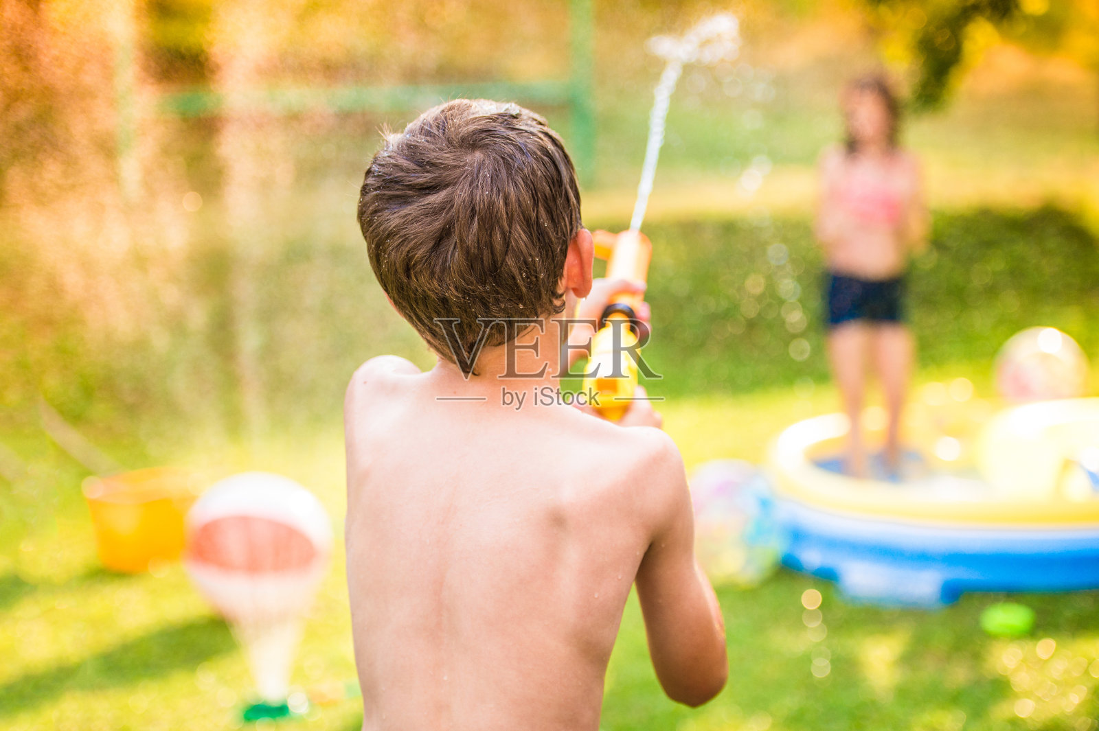 花园游泳池里，男孩用水枪向女孩泼水照片摄影图片