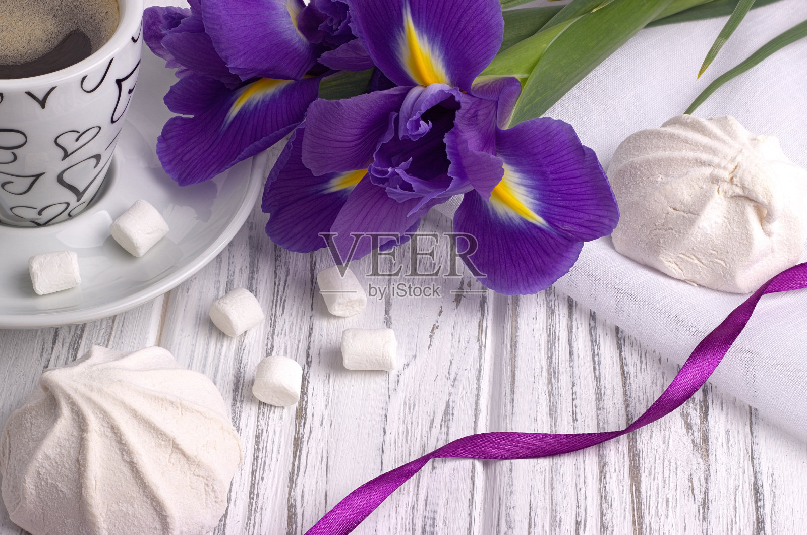 静物与一杯咖啡、棉花糖、蝴蝶花、紫色丝带在白色木制背景。的婚礼。情人节。照片摄影图片