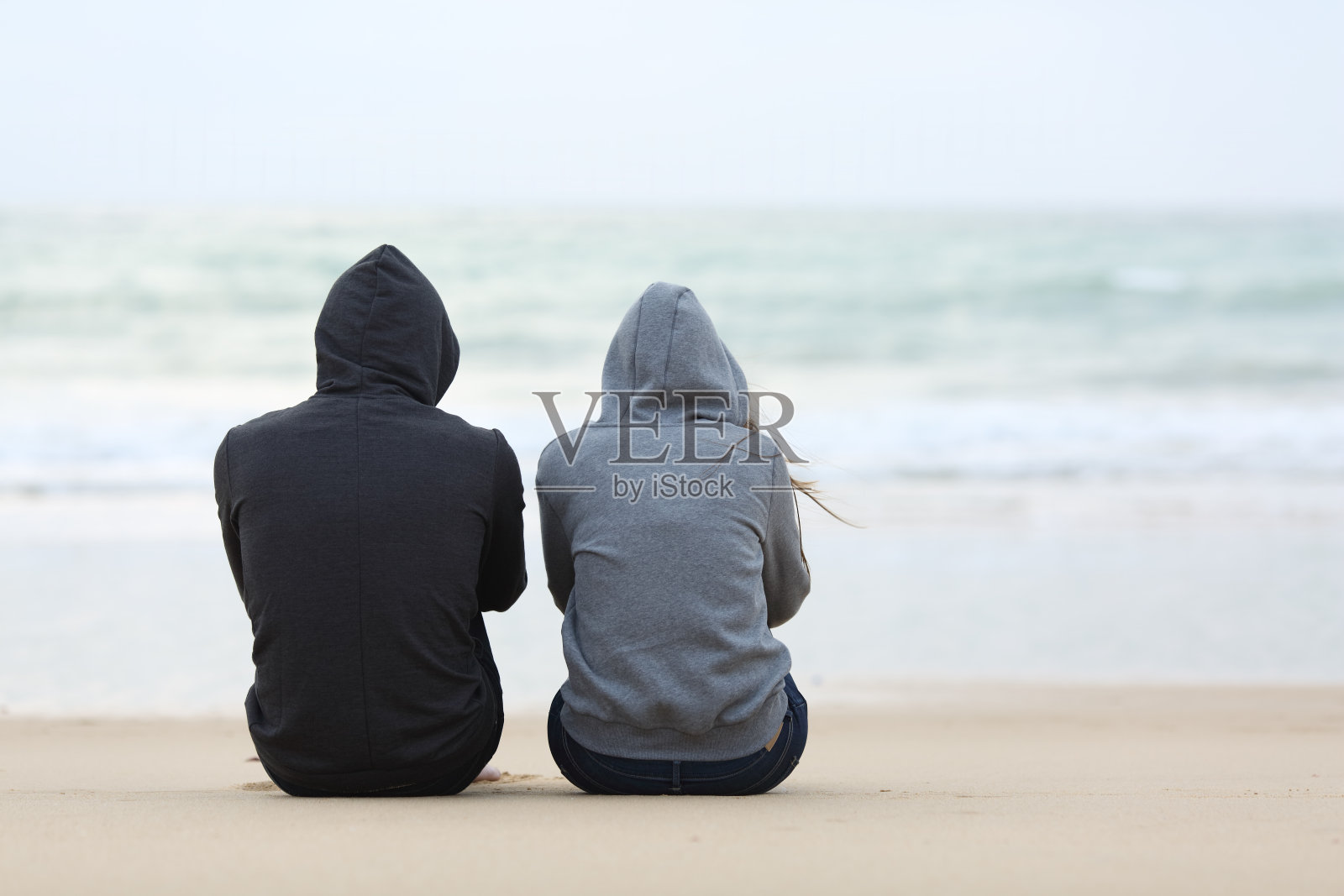 两个悲伤的青少年坐在海滩上照片摄影图片