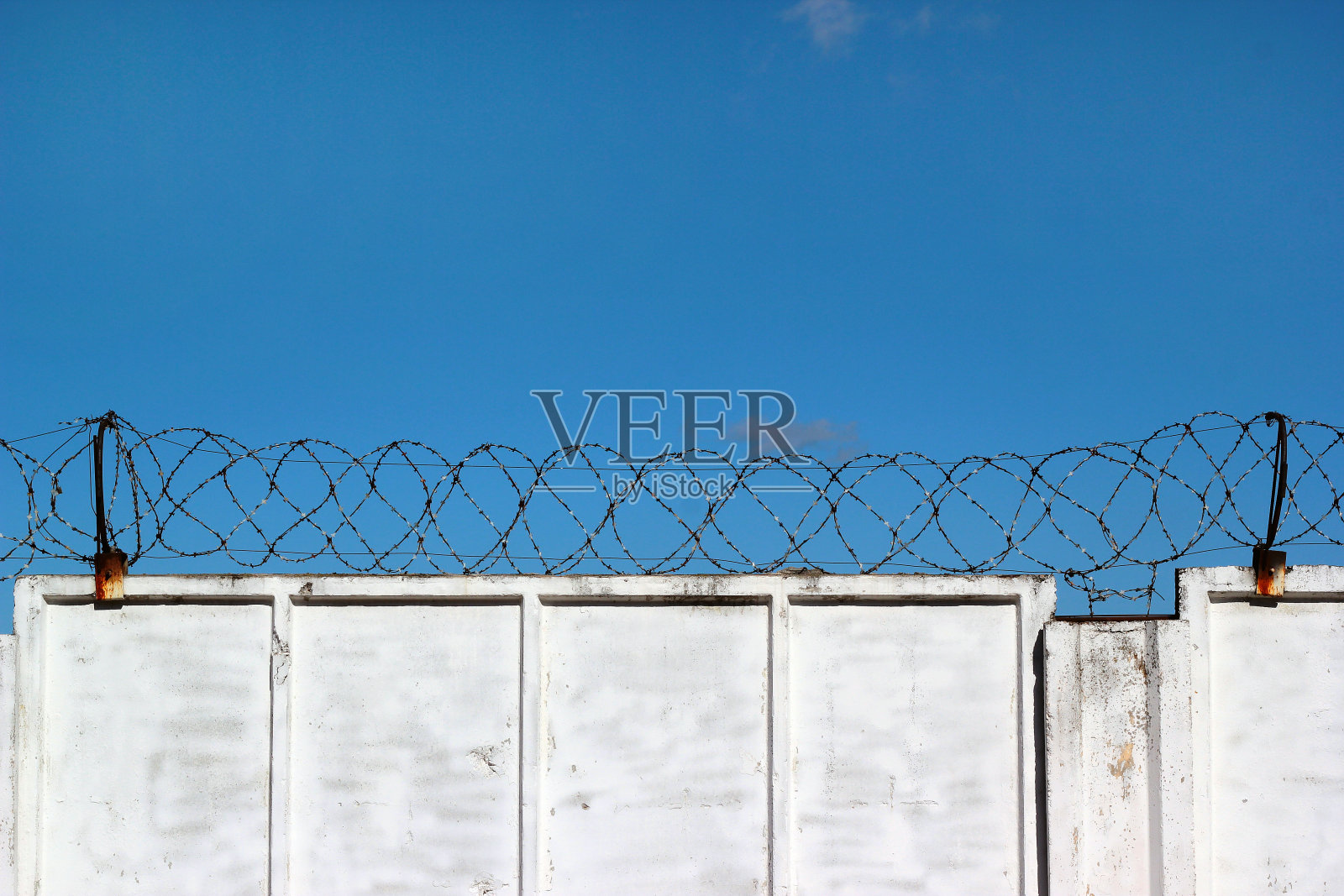 蓝色的天空映衬着白色的混凝土栅栏和带刺的铁丝网照片摄影图片