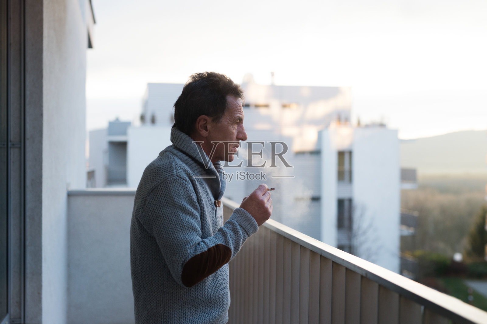 一个严肃的老人站在阳台上，抽着烟照片摄影图片