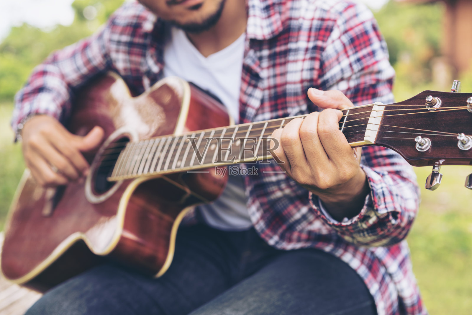 男人的手在弹吉他，坐在绿色的草地上照片摄影图片