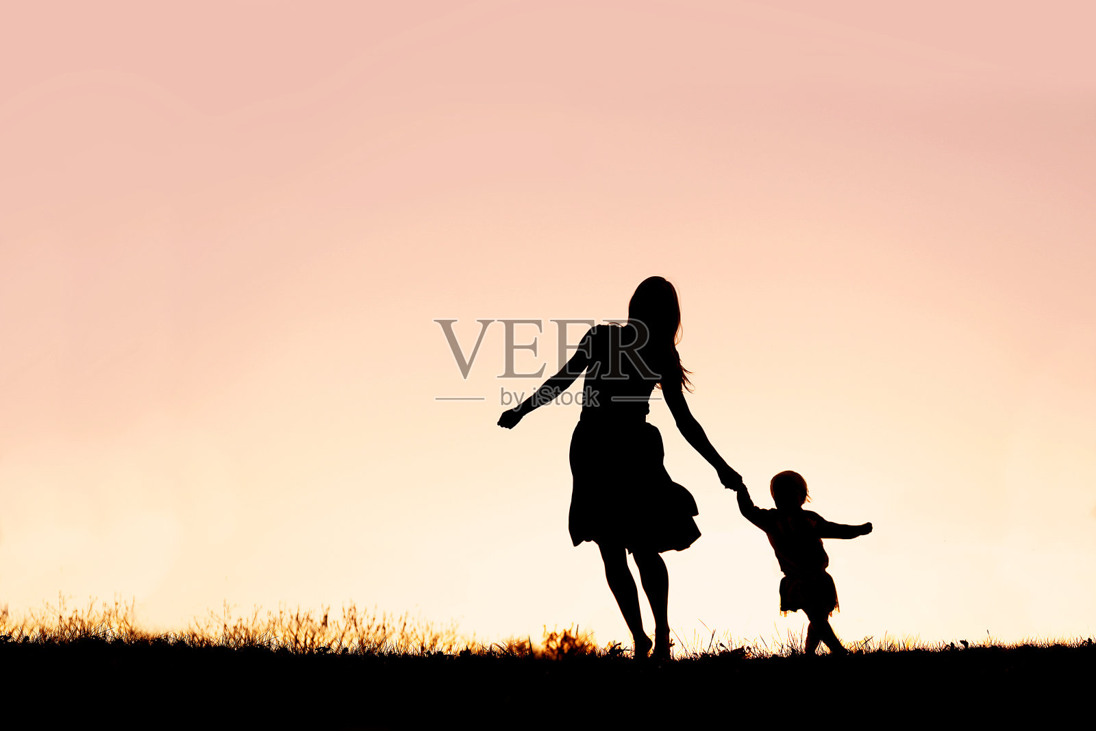 母亲和婴儿女儿在夕阳下奔跑和跳舞的剪影照片摄影图片