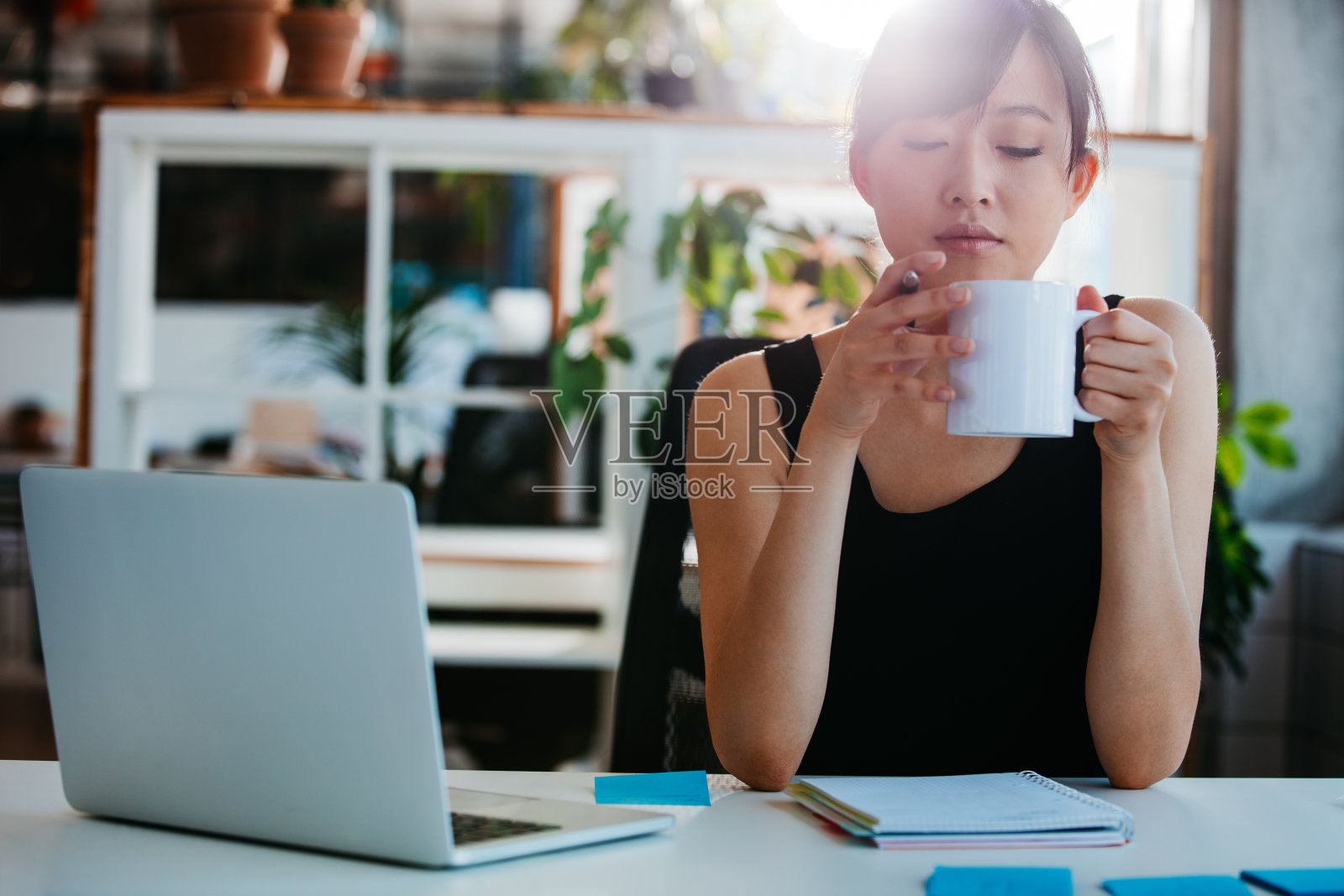 轻松的年轻女子在她的办公桌前喝咖啡照片摄影图片