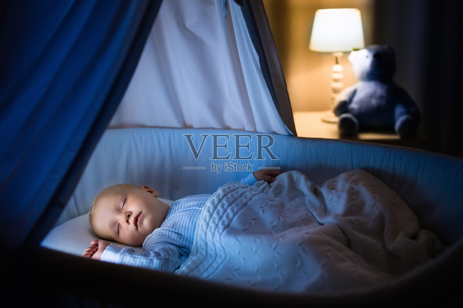 小男孩晚上睡在蓝色的婴儿床里照片摄影图片