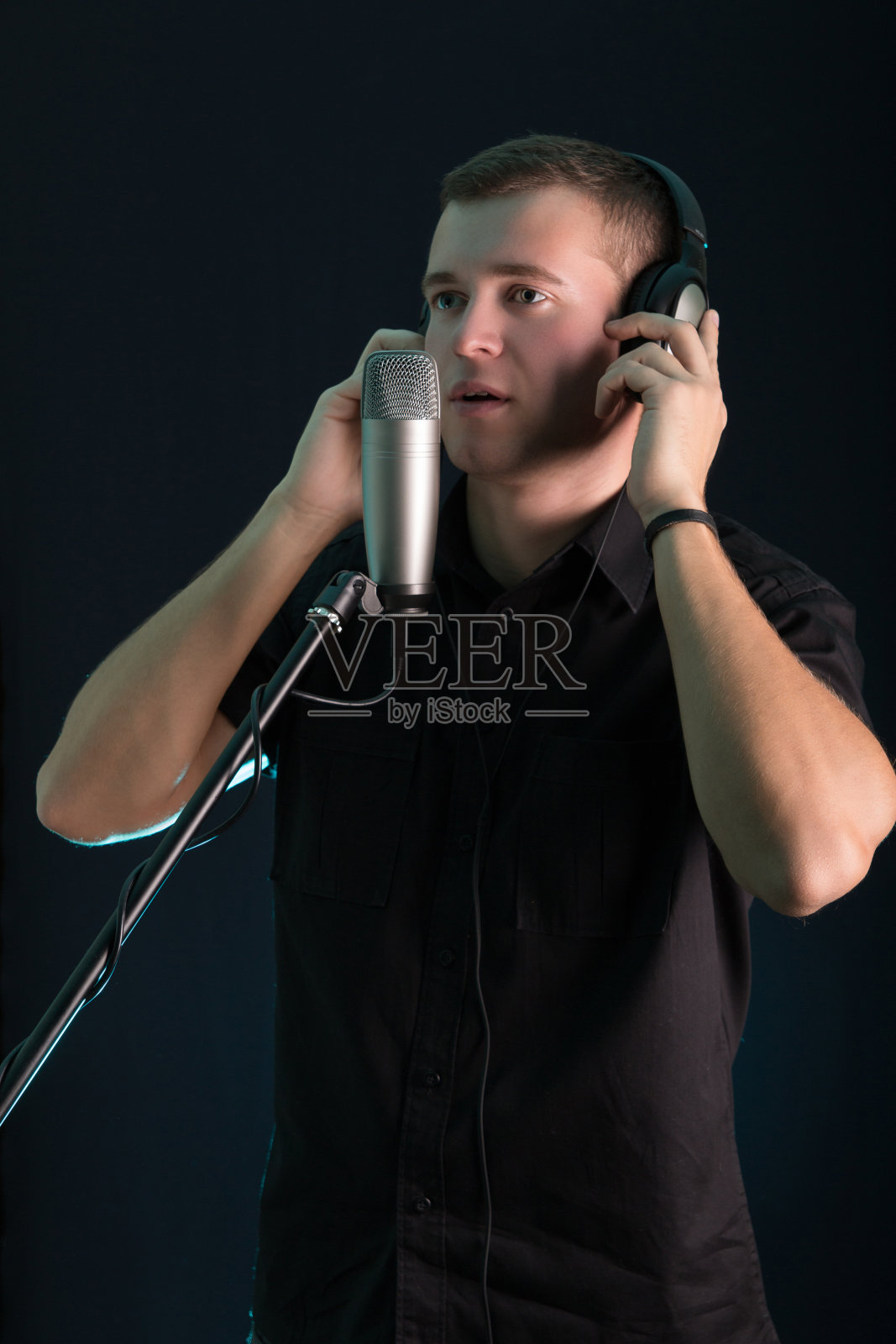 一个年轻人在黑暗的背景下，在录音室的麦克风里唱歌照片摄影图片